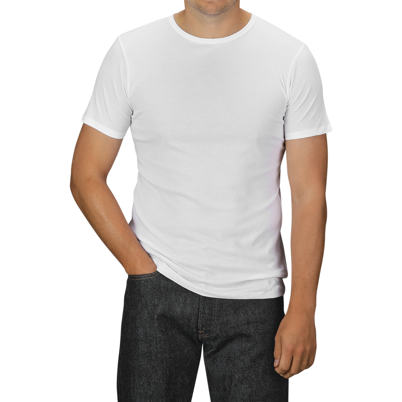 A person wearing a White Pima Cotton Earth T-Shirt by The White Briefs and slim fit dark jeans stands with their left hand in their pocket. The background is a neutral grey.