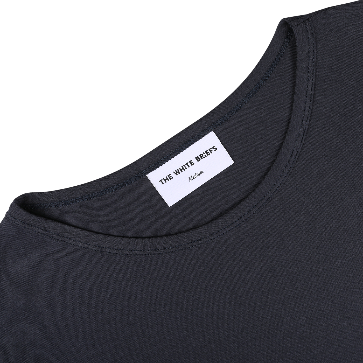 Close-up of a dark-colored Parisian Night Pima Cotton Earth T-Shirt's classic crewneck neckline with a label that reads, "THE WHITE BRIEFS Medium." Made from organic pima cotton, the shirt is on a plain, light-colored background.