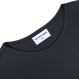 Close-up of a dark-colored Parisian Night Pima Cotton Earth T-Shirt's classic crewneck neckline with a label that reads, "THE WHITE BRIEFS Medium." Made from organic pima cotton, the shirt is on a plain, light-colored background.