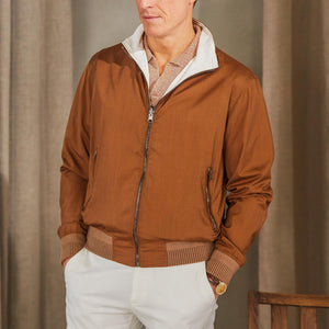 A man wearing a Manto Tobacco Reversible Loro Piana Wool Silk Blouson jacket and white pants.