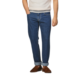 Wearing a white ribbed shirt, slim fit Tramarossa Blue Sky Relax Super Stretch Michelangelo jeans with cuffs, and brown shoes, a person stands against a plain background.