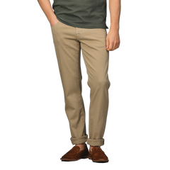 Person wearing a dark green shirt, Tramarossa Desert Beige Super Stretch Michelangelo Jeans, and brown shoes, standing with one hand in pocket.