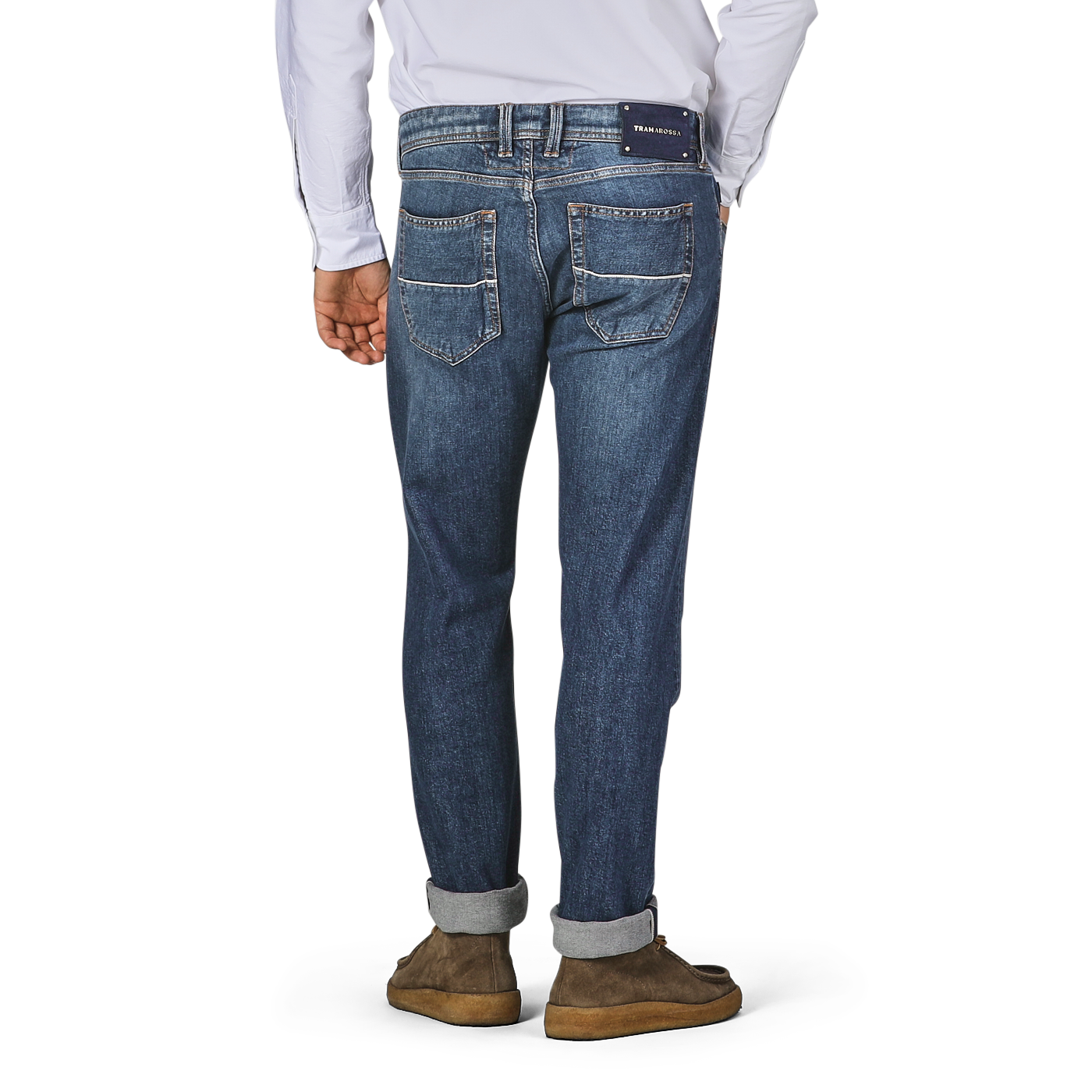 A person is standing with their back to the camera, wearing Tramarossa's Washed Blue Loro Piana Cotton Michealangelo Jeans and brown shoes. The jeans, made from super stretch material, are slightly cuffed at the bottom.