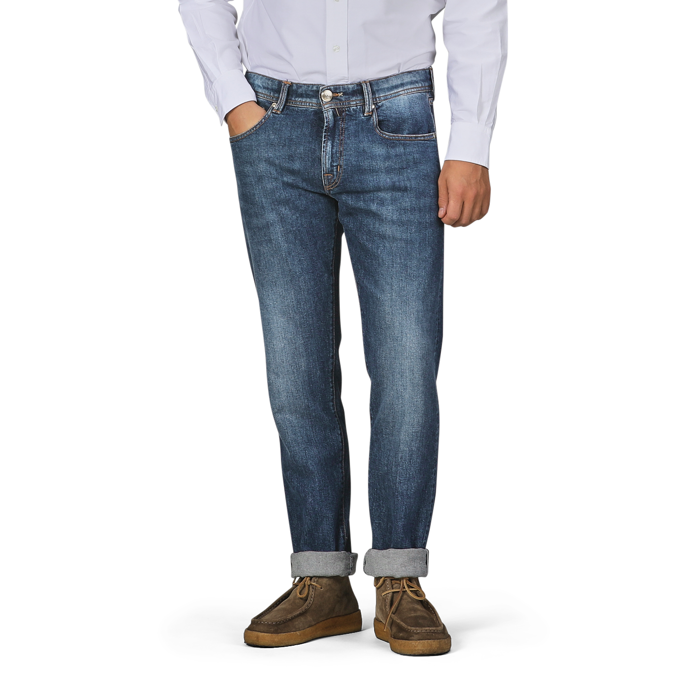 A person wearing a white button-up shirt, Tramarossa's Washed Blue Loro Piana Cotton Michealangelo Jeans with rolled cuffs, and brown shoes stands with one hand in their pocket against a plain backdrop.