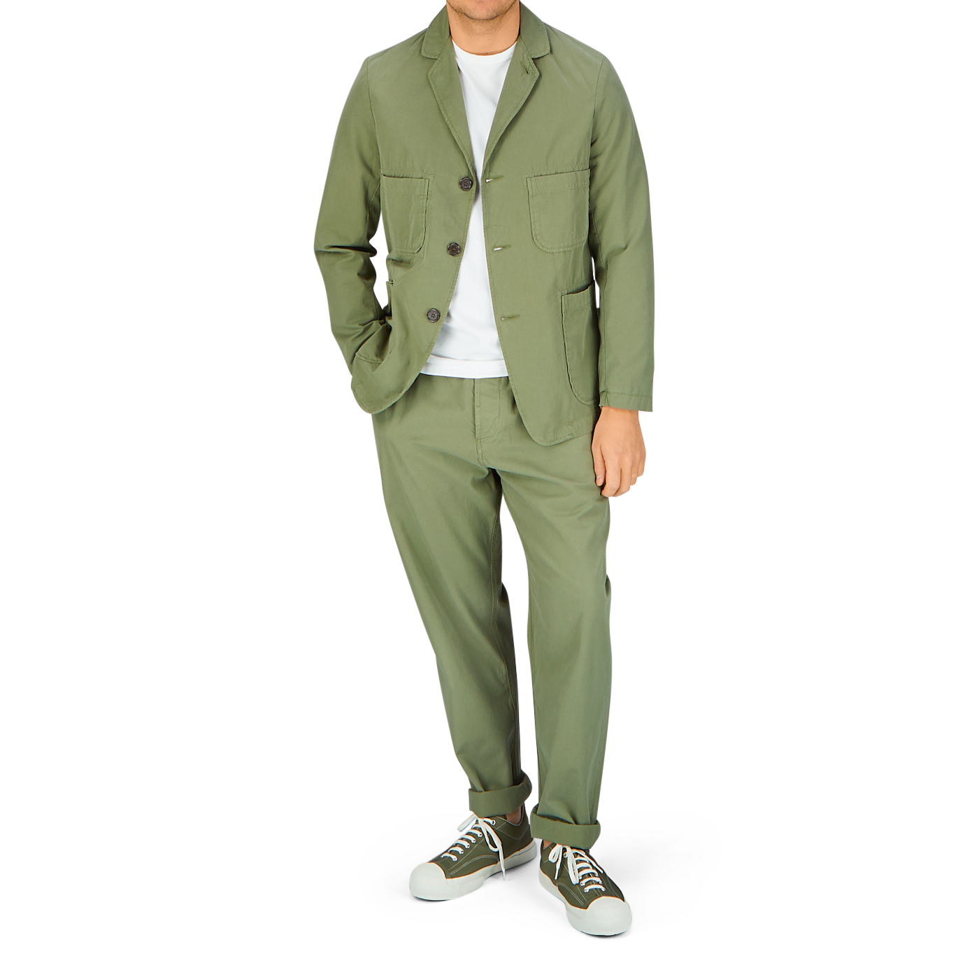 Man in a Universal Works Birch Green Cotton Summer Canvas 5-Pocket Jacket with a white t-shirt and sneakers standing against a light background.