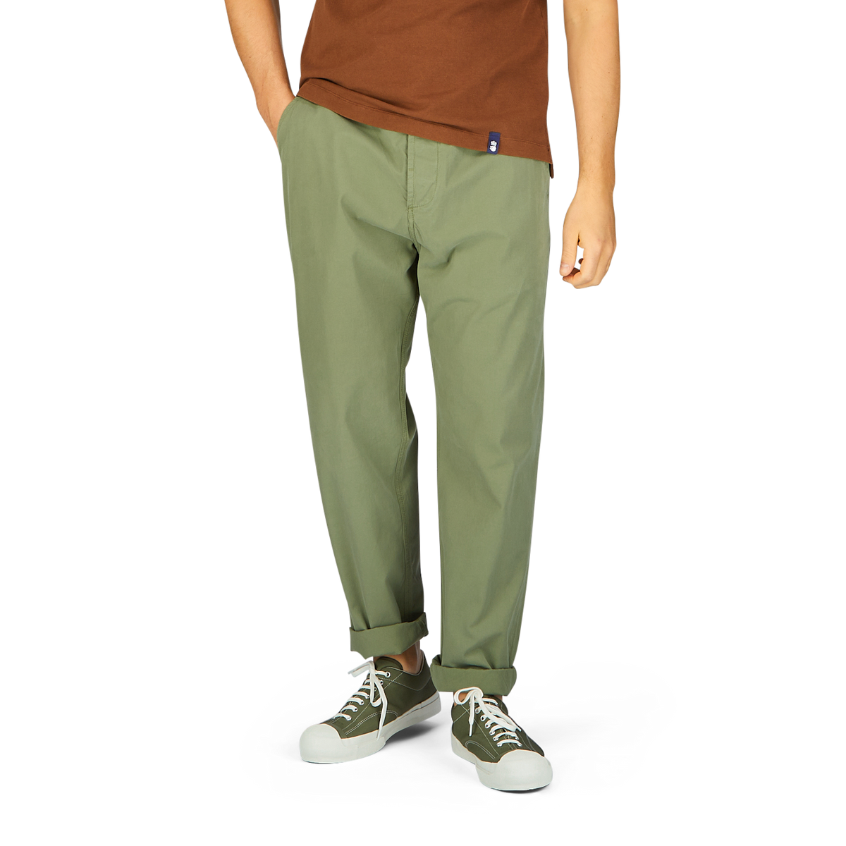 A person wearing Universal Works Birch Green Cotton Summer Canvas Military Chinos and white sneakers stands against a plain background.