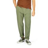 A person wearing Universal Works Birch Green Cotton Summer Canvas Military Chinos and white sneakers stands against a plain background.