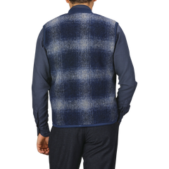 Back view of a person wearing a Blue-Grey Fresco Fleece Zip Waistcoat by Universal Works over a dark blue shirt and dark pants, standing against a plain light gray background.