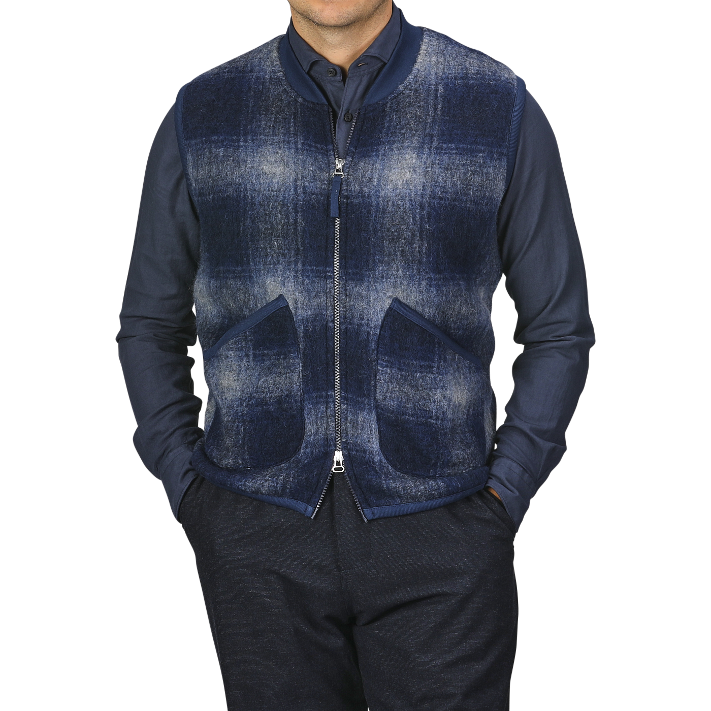 A person wearing a navy blue shirt and a Blue-Grey Fresco Fleece Zip Waistcoat by Universal Works, which serves as a perfect layering piece with two front pockets, stands against a plain background.