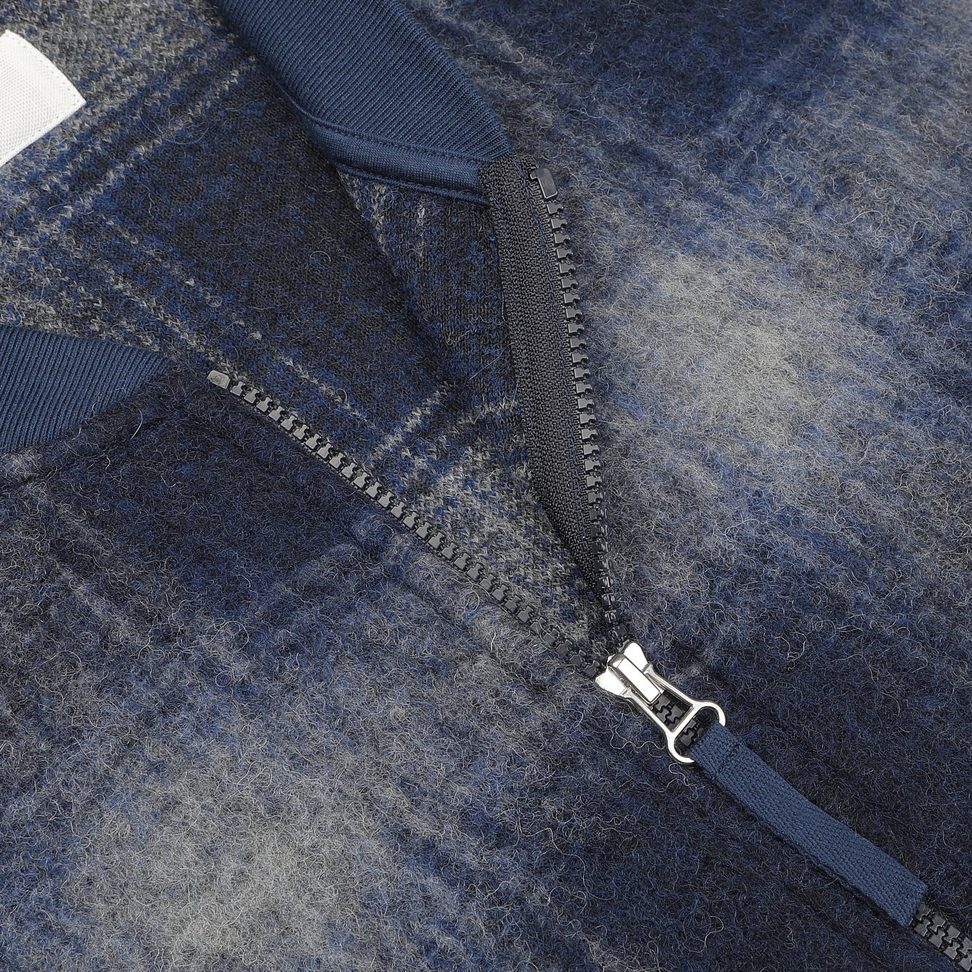 Close-up of a partially unzipped blue and grey plaid fabric with a visible zipper and navy blue collar, perfect as a layering piece for your Universal Works Blue-Grey Fresco Fleece Zip Waistcoat.