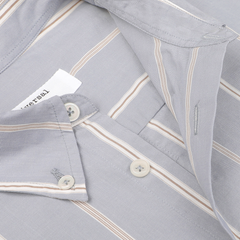 Close-up of a light gray, blue-striped Blue Sydney Striped Cotton Lazy Day Shirt by Universal Works, featuring beige and white accents, showcasing buttons and buttonholes on the collar and a partially visible tag.