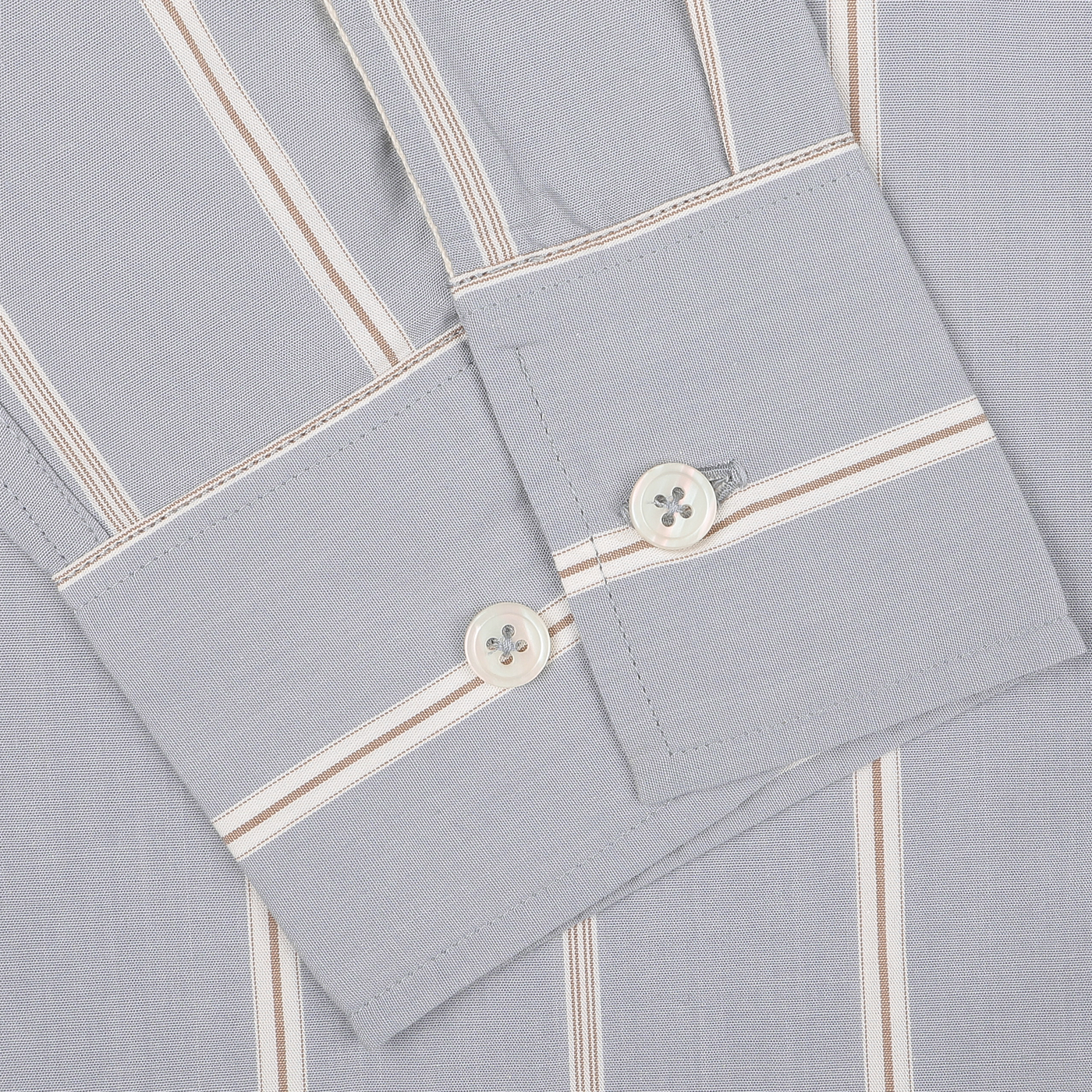 Close-up of the sleeve cuff of the Blue Sydney Striped Cotton Lazy Day Shirt by Universal Works, showcasing tan and white vertical stripes with two white buttons.