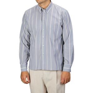 A man wearing a Universal Works Blue Sydney Striped Cotton Lazy Day Shirt with beige pants stands against a plain background. His face is not visible.