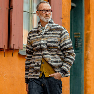 A man wearing glasses and a Universal Works Brown Fair Isle Wool New York Button Cardigan standing in front of a building.