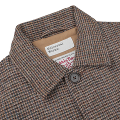 Close-up of a checked Brown Melange Harris Tweed Bakers C Jacket with a buttoned collar, displaying the Universal Works and Harris Tweed labels, indicating it is made from hand-woven cloth.