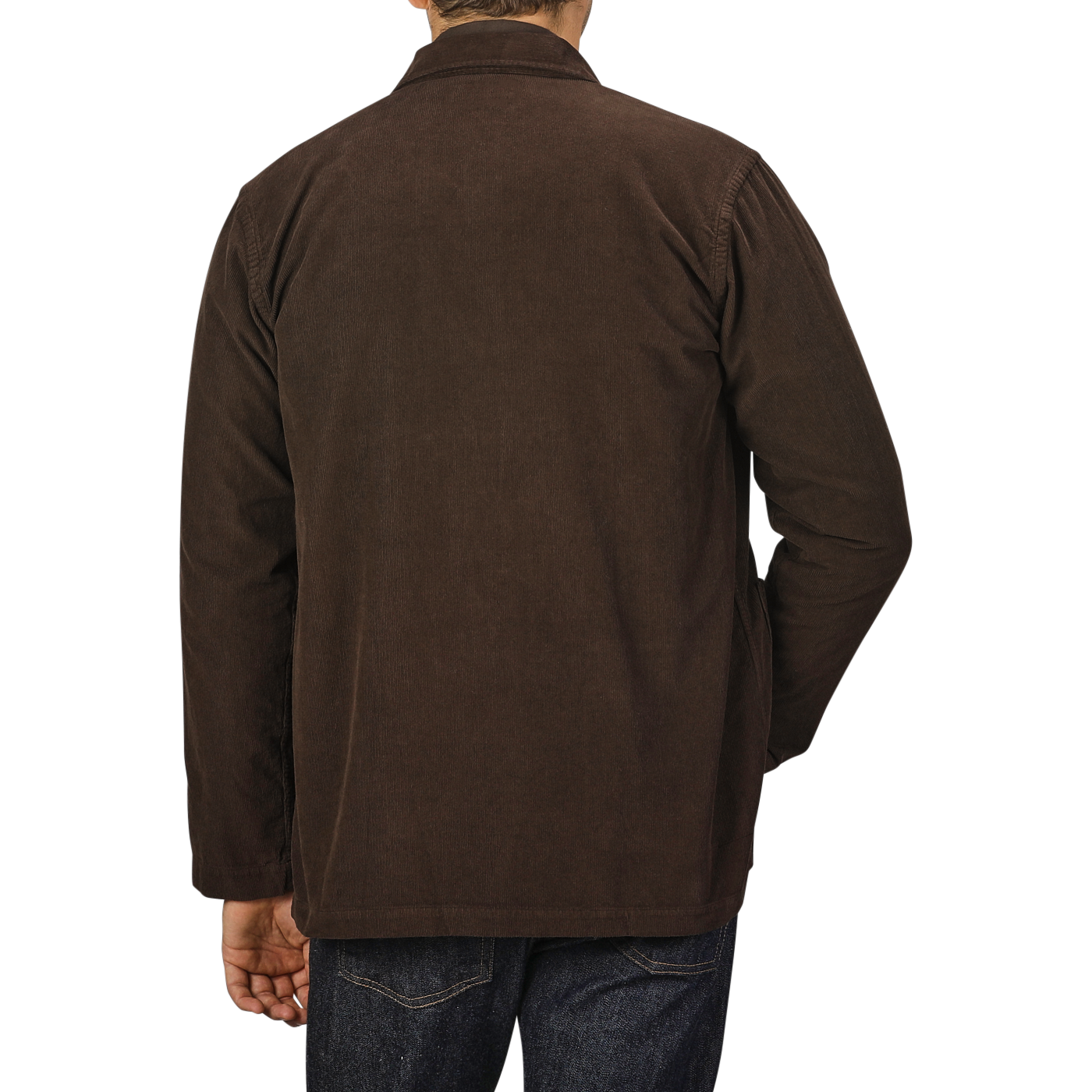 A person is wearing a Dark Brown Fine Corduroy Bakers Overshirt from Universal Works and blue jeans, viewed from behind against a grey background.