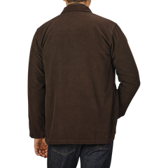 A person is wearing a Dark Brown Fine Corduroy Bakers Overshirt from Universal Works and blue jeans, viewed from behind against a grey background.