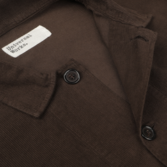 Close-up of the Dark Brown Fine Corduroy Bakers Overshirt by Universal Works, featuring two black buttons and a tag labeled "Universal Works.