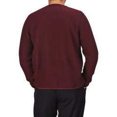 A person wearing the Deep Red Wool Fleece Cardigan from Universal Works and black pants is shown from the back. The background is plain and light-colored.