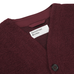 Close-up of the Deep Red Wool Fleece Cardigan with a V-neckline, featuring a white label reading "Universal Works" and black buttons.