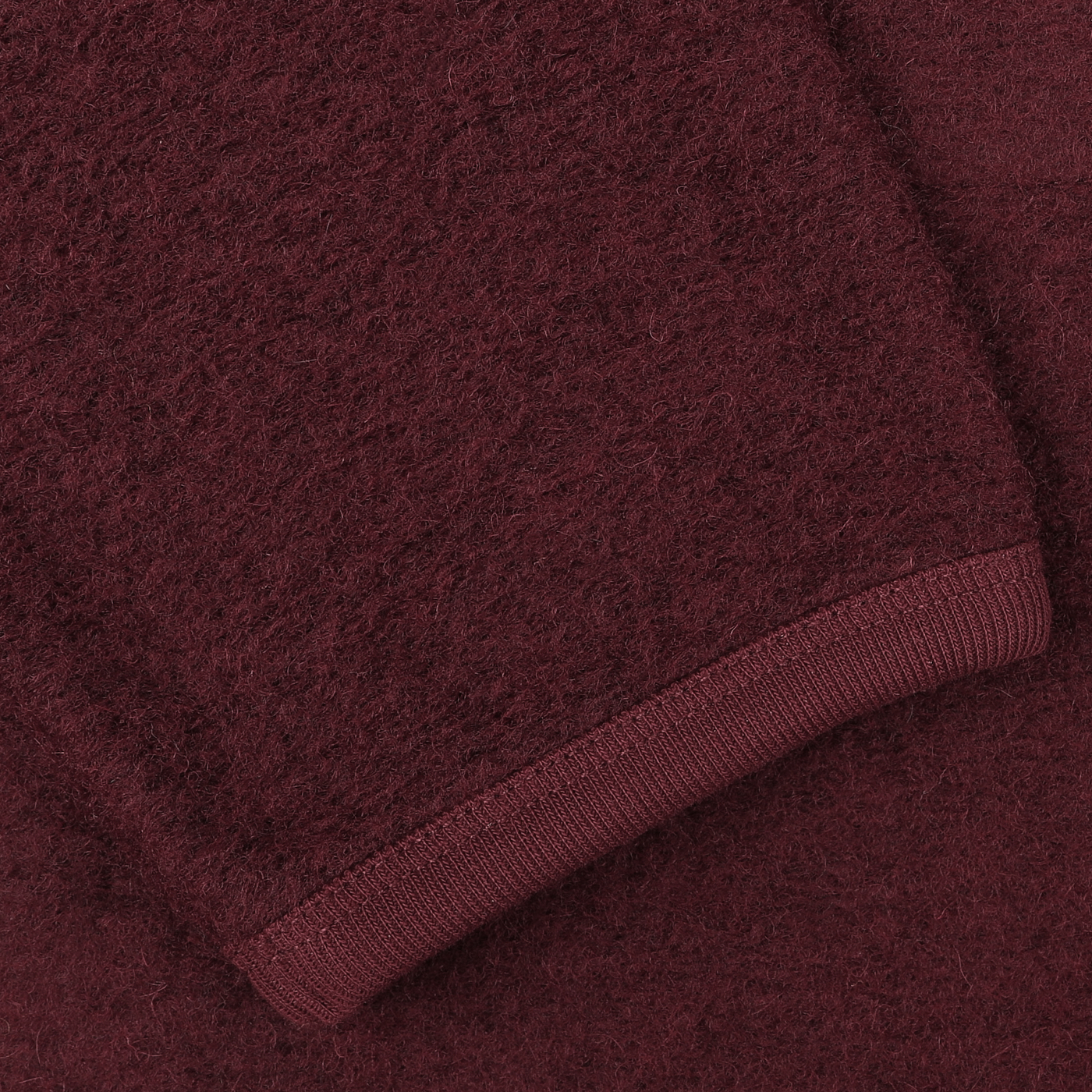 Close-up view of a dark red, fuzzy-textured fabric from the Universal Works Deep Red Wool Fleece Cardigan, focusing on a folded sleeve with ribbed cuffs.