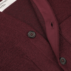 Close-up of a Deep Red Wool Fleece Cardigan by Universal Works, highlighting the fabric texture, buttons, and a partially visible white clothing label.