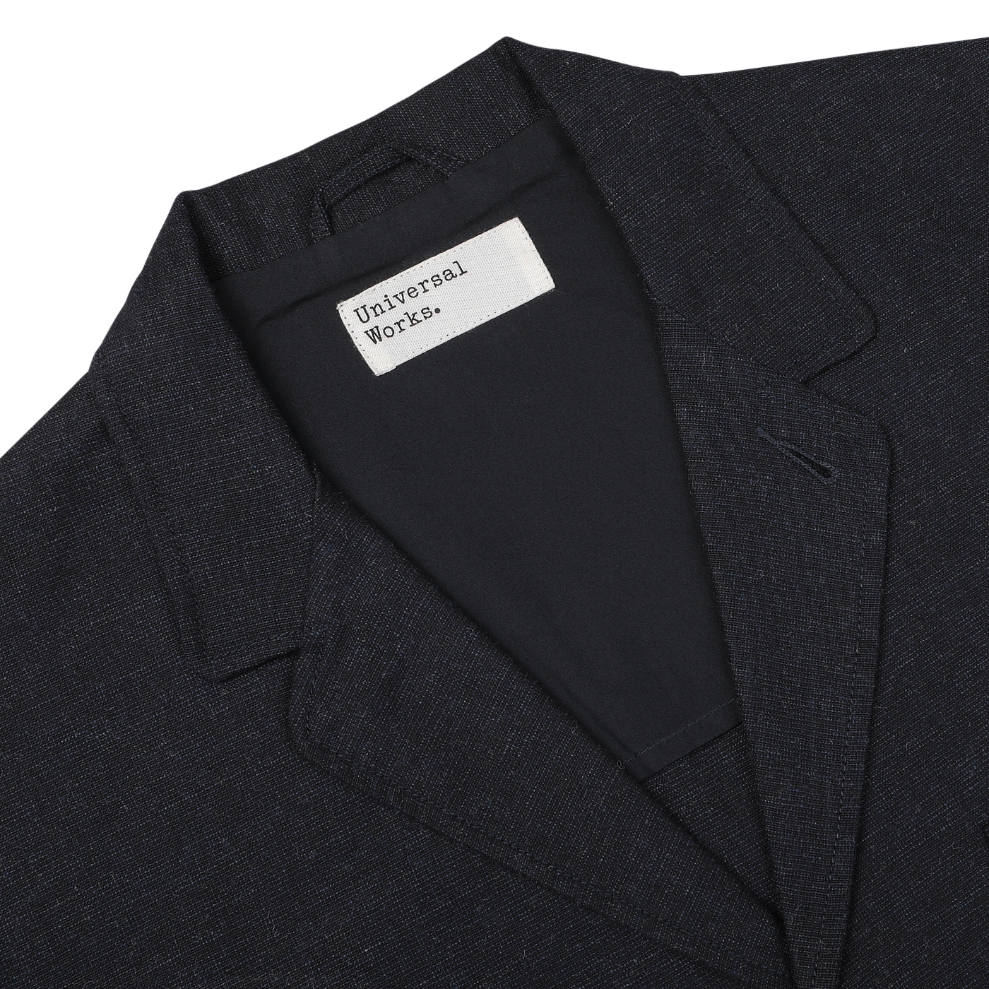 A close-up of a Navy Blue Birdseye Tweed 3 Button Jacket with a white tag reading "Universal Works" sewn on the inside near the collar.