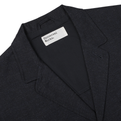 A close-up of a Navy Blue Birdseye Tweed 3 Button Jacket with a white tag reading "Universal Works" sewn on the inside near the collar.