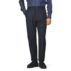 Person wearing a blue shirt, Universal Works Navy Blue Birdseye Tweed Military Chinos, and black shoes, standing with one hand in their pocket.