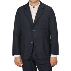 A man wearing the Universal Works Navy Blue Upcycled Tweed 2 Button Jacket over a light-colored shirt, standing against a plain gray background. The sleek design features three front pockets and is crafted from upcycled wool tweed, merging modern style with sustainable fashion.