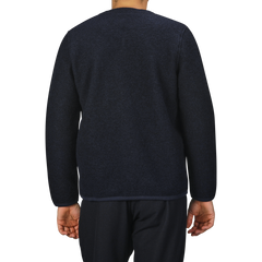 A person wearing a Navy Blue Wool Fleece Cardigan from Universal Works and navy blue pants stands with their back to the camera against a plain background, reminiscent of the brand's minimalist designs.