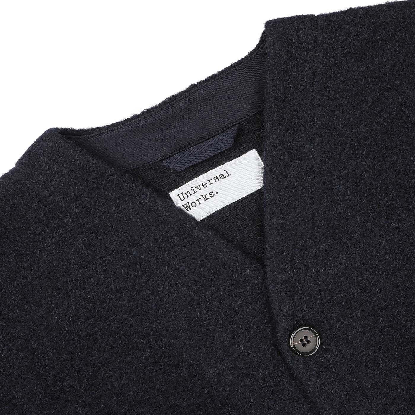 Close-up of a Navy Blue Wool Fleece Cardigan from Universal Works, showcasing its button and the white label near the neckline that reads "Universal Works.