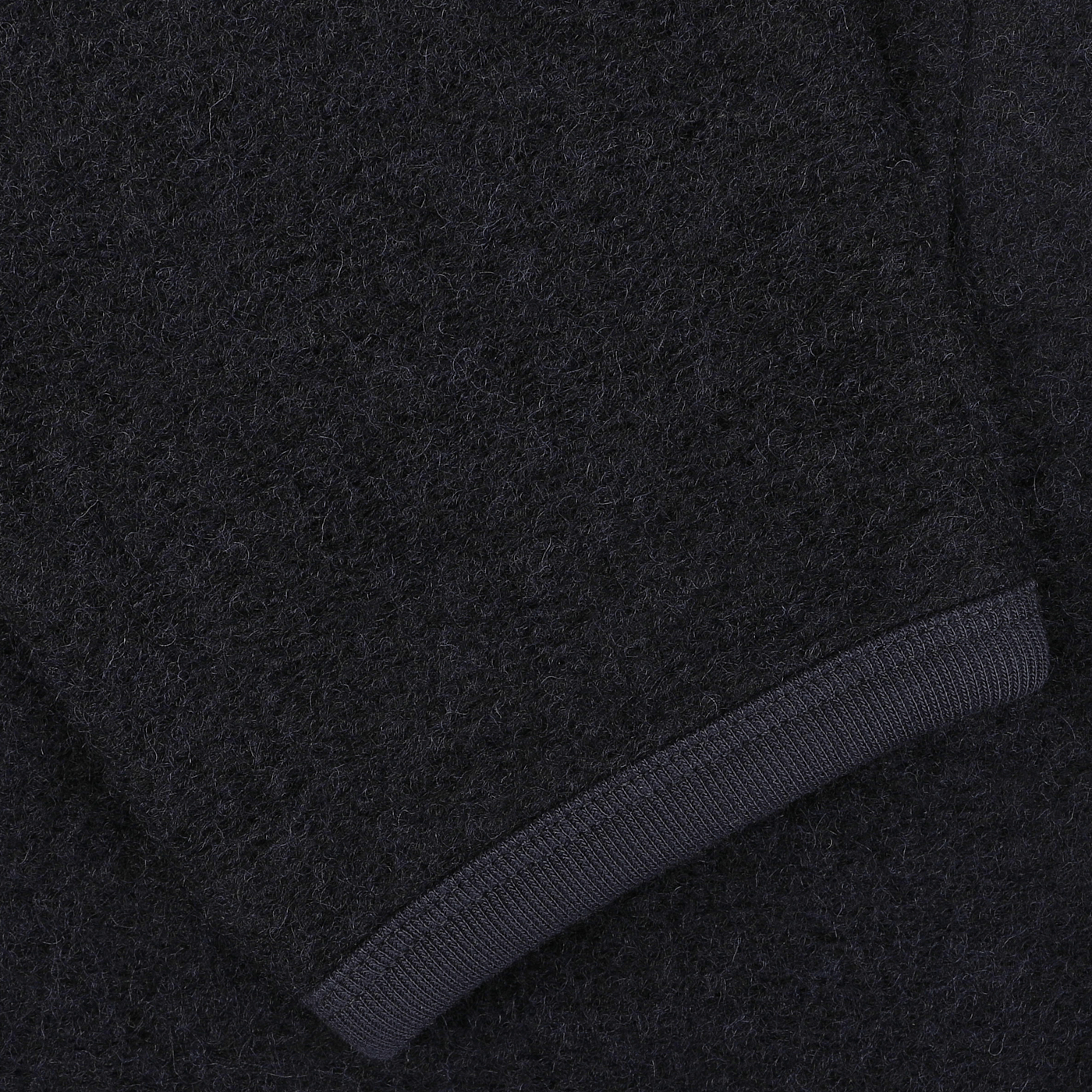 Close-up of a dark gray woolen fabric with a soft, fuzzy texture and visible stitching detail on the edge, reminiscent of the craftsmanship found in a Universal Works Navy Blue Wool Fleece Cardigan.