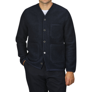 A person wearing a Navy Blue Wool Fleece Cardigan by Universal Works, featuring three pockets, stands against a plain background. They are also dressed in dark pants. Only the torso, part of the arms, and neck are visible.