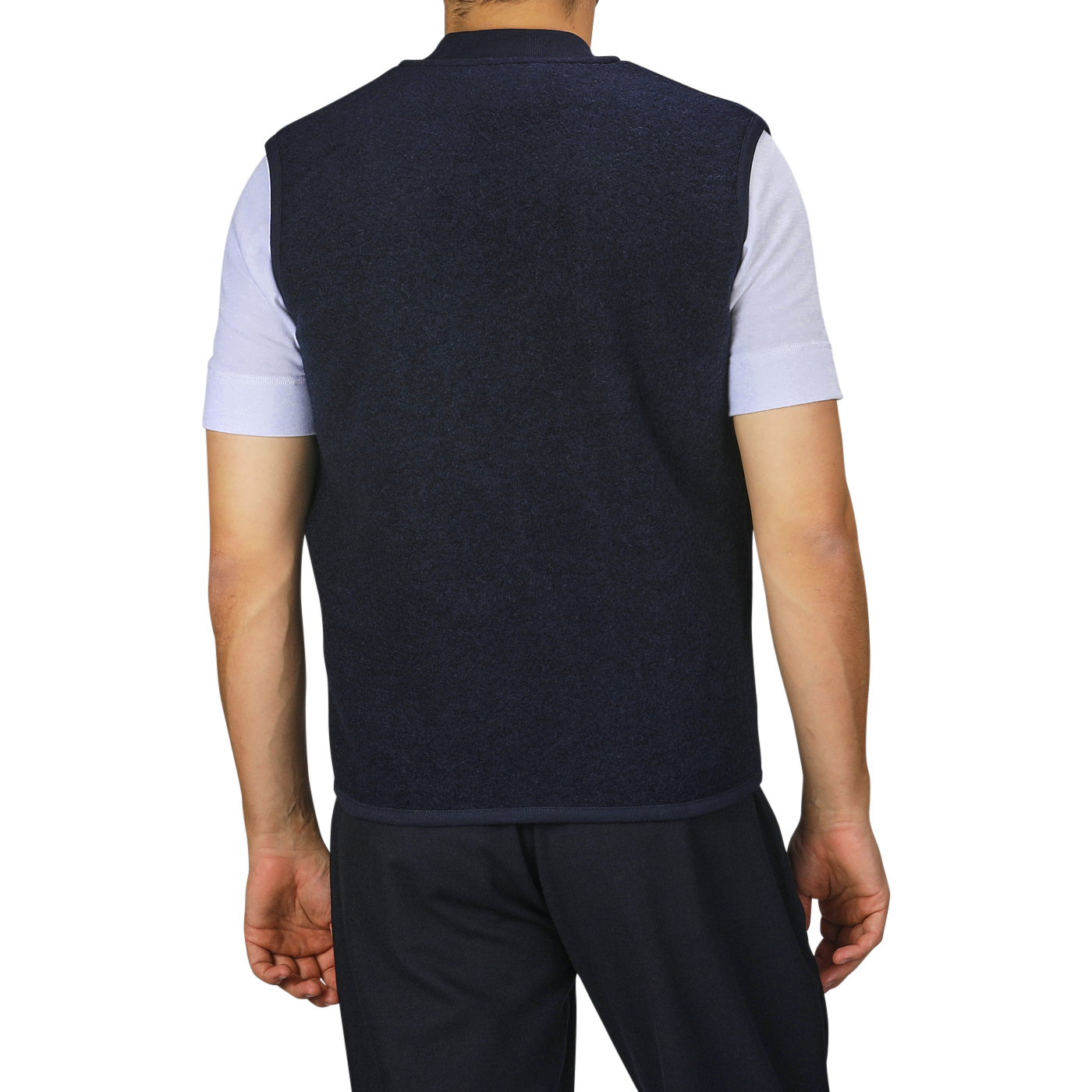 A person is standing with their back to the camera, wearing a Navy Blue Wool Fleece Zip Waistcoat by Universal Works over a light short-sleeve shirt and dark pants.