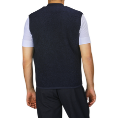 A person is standing with their back to the camera, wearing a Navy Blue Wool Fleece Zip Waistcoat by Universal Works over a light short-sleeve shirt and dark pants.