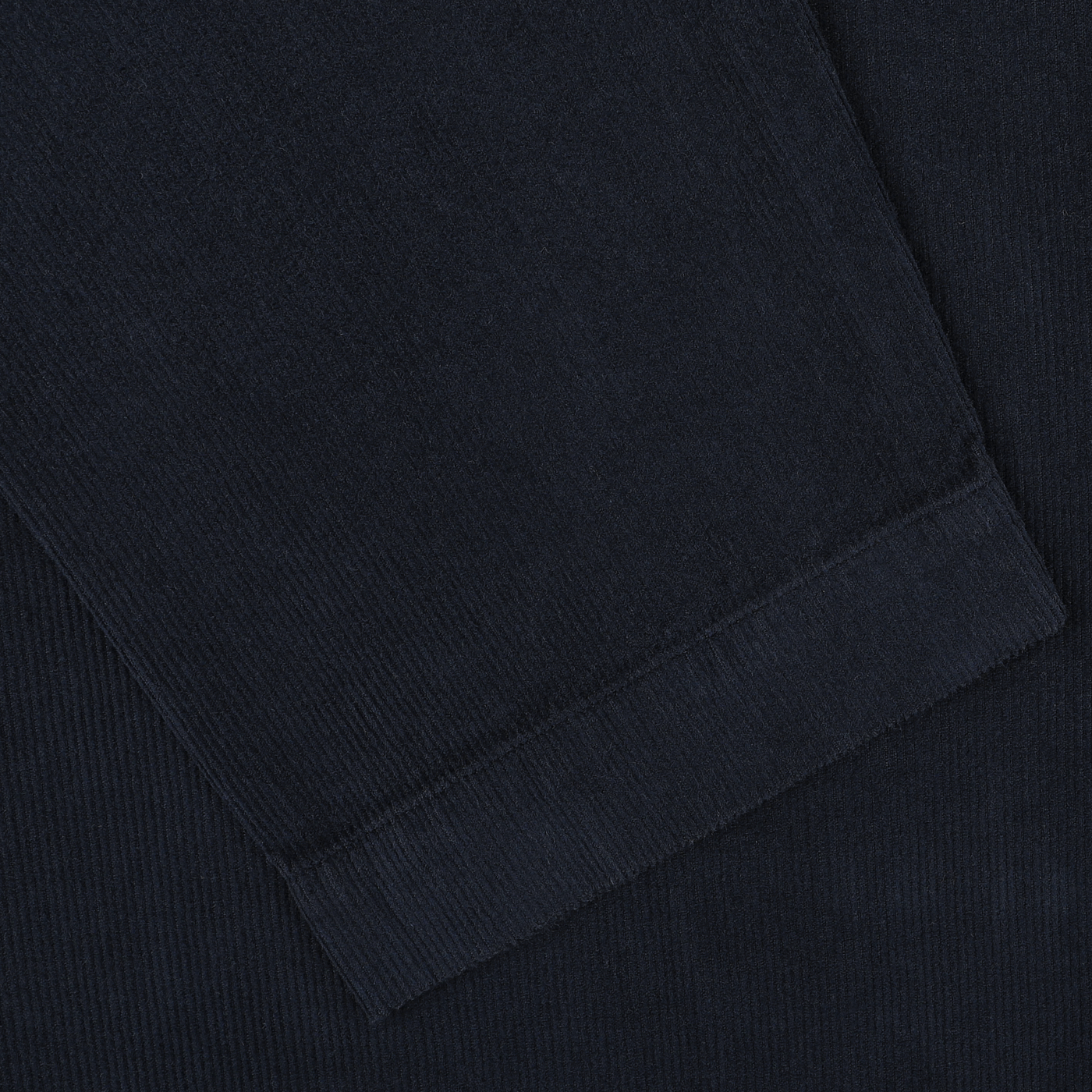 A close-up view of the Navy Fine Corduroy Bakers Overshirt by Universal Works, showcasing its dark navy blue cotton corduroy fabric with visible texture and detailed stitching along the edge.