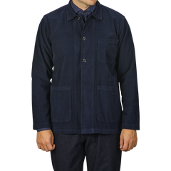 A person wearing the Universal Works Navy Fine Corduroy Bakers Overshirt, which is buttoned-up and features three pockets, paired with matching dark blue pants. The image is cropped at the neck and thighs.