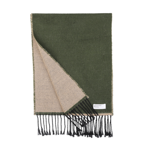 An olive-green and beige, double-sided seasonal scarf with black fringed ends, partially folded to reveal both sides. A small white label on the scarf reads "Universal Works." Made in Italy, this stylish accessory adds a touch of elegance to your winter wardrobe and is known as the Grass Beige Double-Sided Acrylic Scarf.