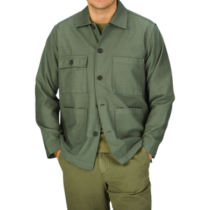 Man wearing a green Universal Works Olive Green Cotton Sateen Dockside Jacket with pockets standing against a gray background.