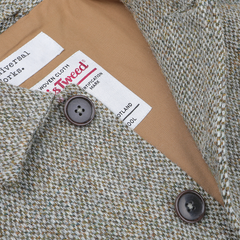 Close-up of the Olive Melange Harris Tweed Bakers C Jacket by Universal Works, featuring a brown and white houndstooth pattern, two brown buttons, and an inside label with branding and care information.