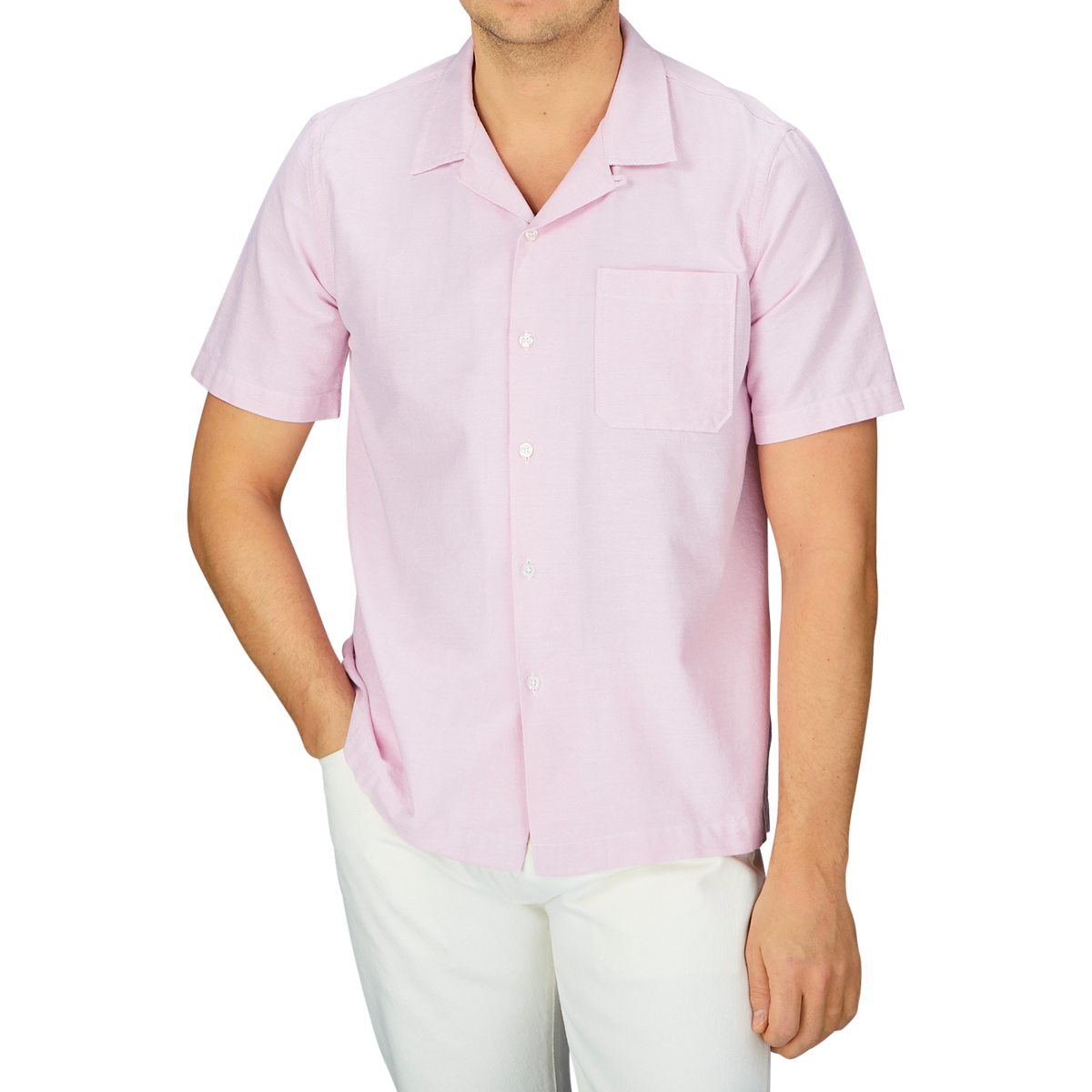 A man wearing a Universal Works Pink Cotton Oxford Camp Collar Road Shirt with white pants.