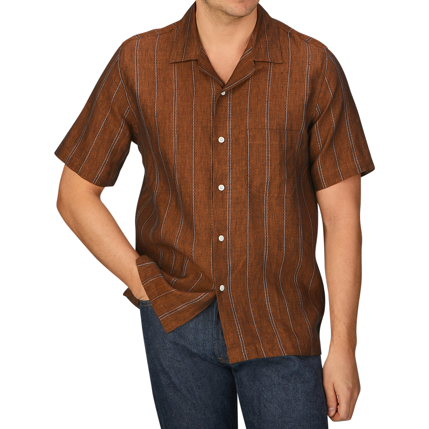 A man wearing a Rust Brown Striped Linen Road Universal Works camp collar shirt and jeans.