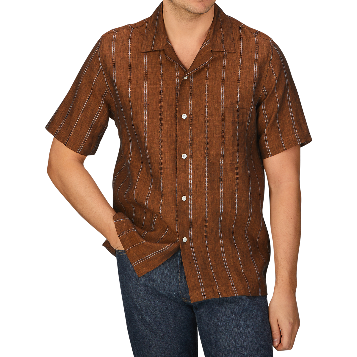 A man wearing a Rust Brown Striped Linen Road Universal Works camp collar shirt and jeans.