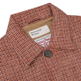 Close-up view of a Rust Orange Harris Tweed Bakers C Jacket with a label that reads "Universal Works." The chore jacket features a buttoned front.