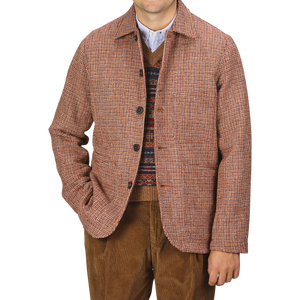 Person wearing a Rust Orange Harris Tweed Bakers C Jacket by Universal Works over a patterned sweater and brown pants, standing against a plain background.