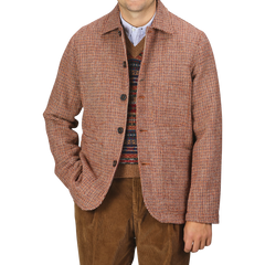 Person wearing a Rust Orange Harris Tweed Bakers C Jacket by Universal Works over a patterned sweater and brown pants, standing against a plain background.