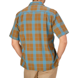 The back view of a man wearing a Seasand Taki Check Cotton Camp Collar Shirt by Universal Works in plaid.