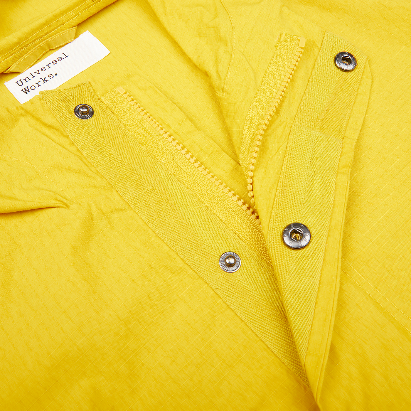 A close up of a yellow, water-resistant Universal Works Stanedge Jacket with zippers.