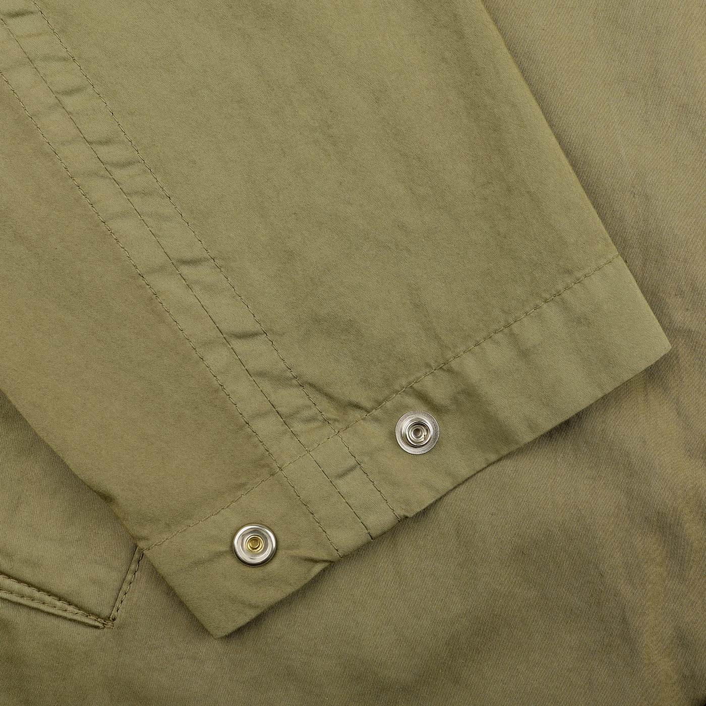 Close-up of the Valstar Green Soft Cotton Nylon Coach Jacket fabric, featuring two metal eyelets and a stitched seam reminiscent of a classic design.